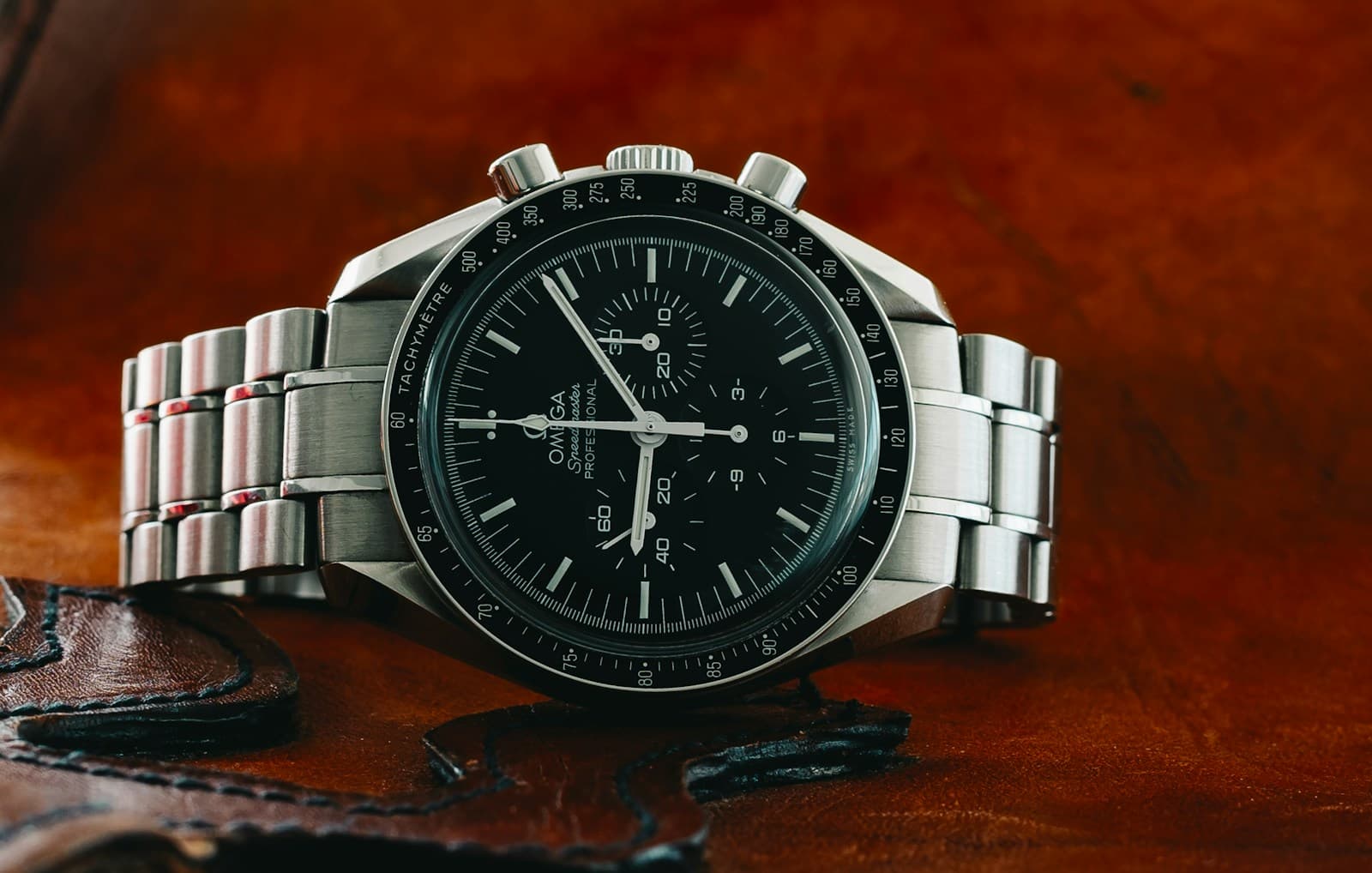 Omega Speedmaster with a black chronograph dial and steel bracelet, photographed on brown leather